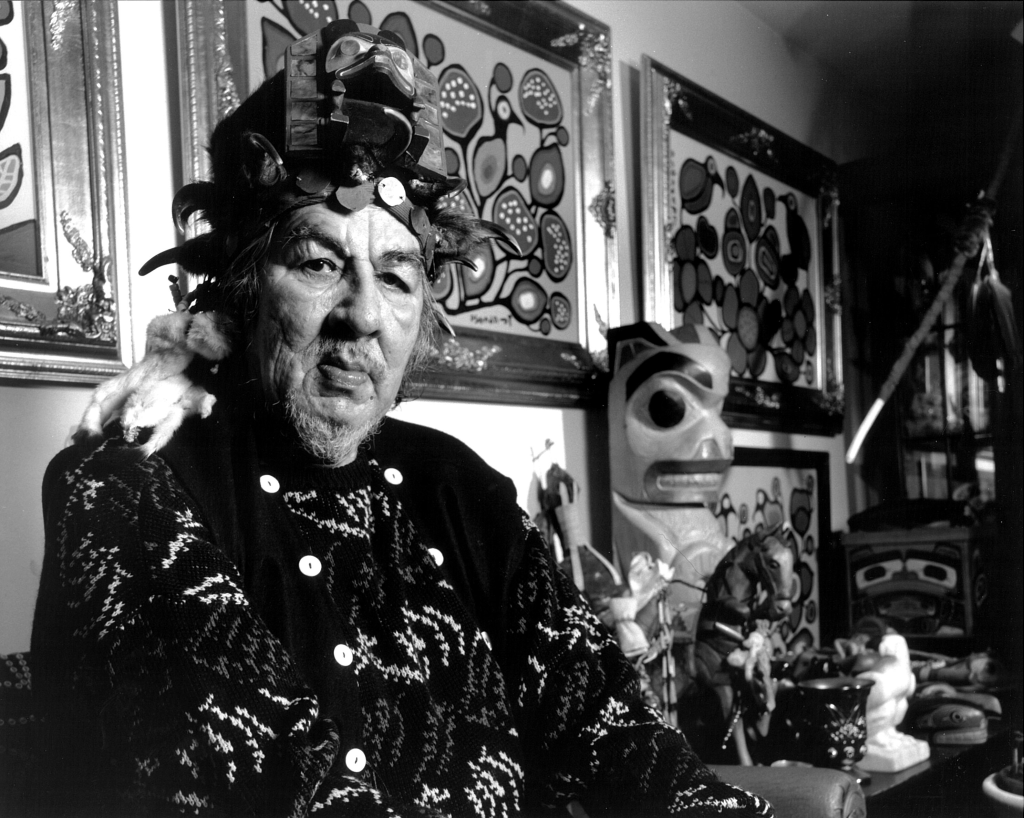 Photograph of Norval Morrisseau surrounded by his collections and possessions