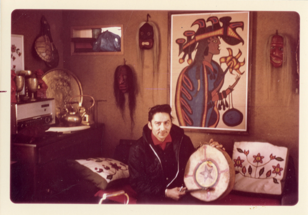 A photograph of Morrisseau in his home, with some of his paintings