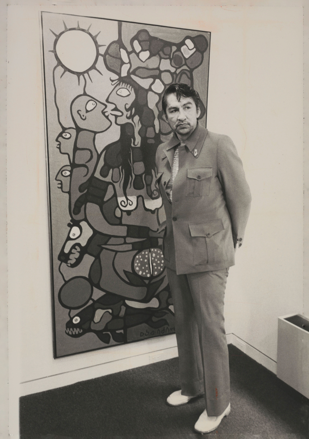 Photograph of Morrisseau posing in front of a painting