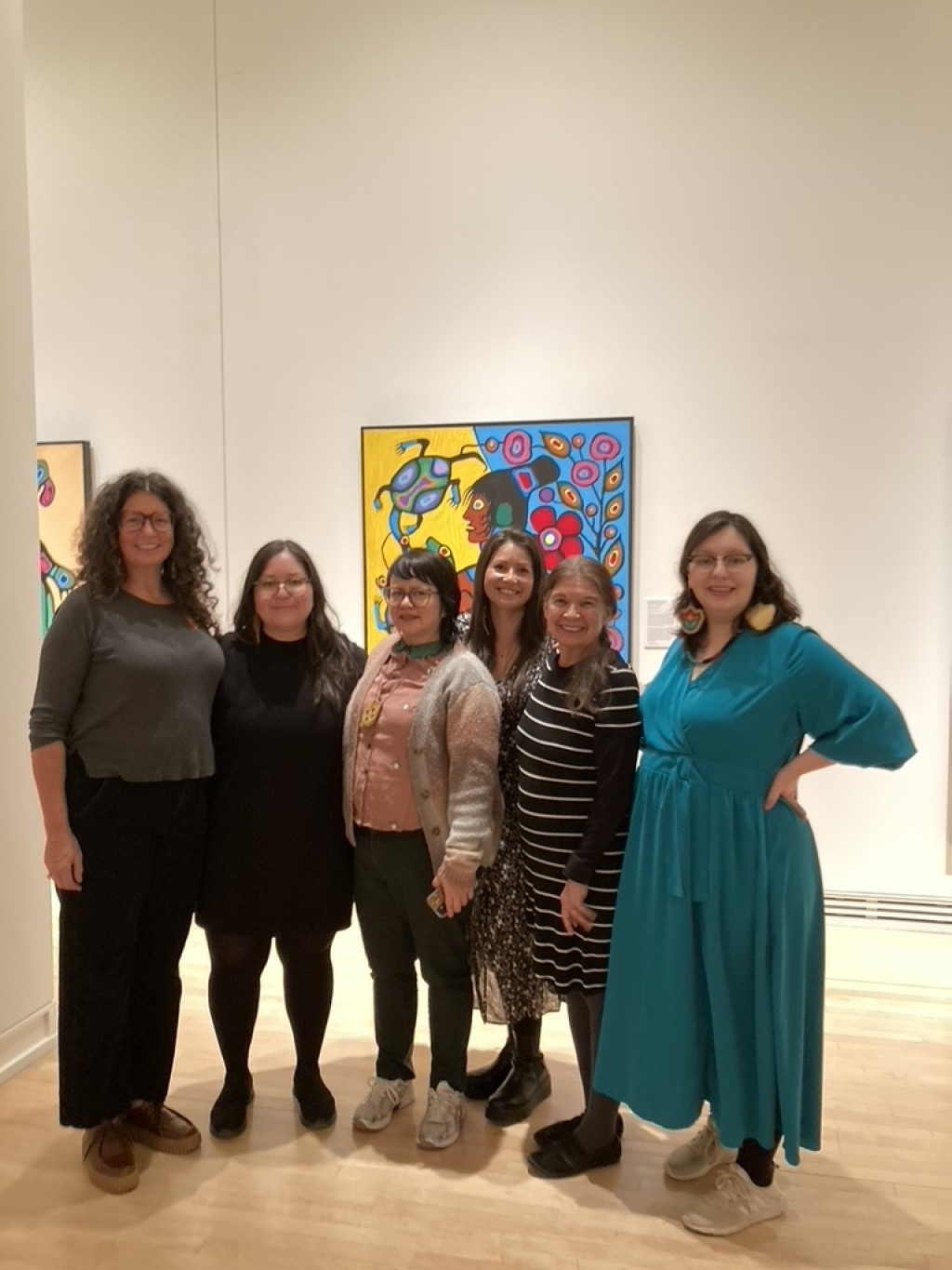 Photograph of 7 female artists in front of Morrisseau's painting in a gallery
